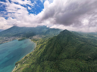 Aerial panoramic view of Lake Atitlán and San Pedro in Guatemala with volcanic mountains, lush green landscape, and dramatic sky over Central America