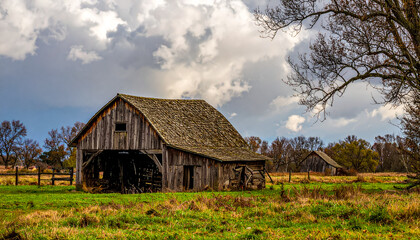 Obraz premium Rustic Wooden Barn in a Grassy Field Under Cloudy Sky