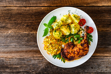 Oven roasted chicken leg with boiled potatoes and young cabbage salad on wooden table
