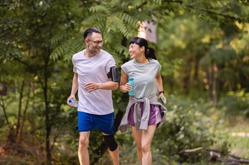 Fototapeta premium Happy diverse couple jogging outdoors in a park, smiling and enjoying an active lifestyle together on a sunny day