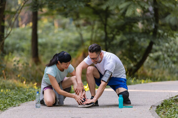 Man helping woman with an injured ankle while jogging in a park, showing care and support during outdoor exercise
