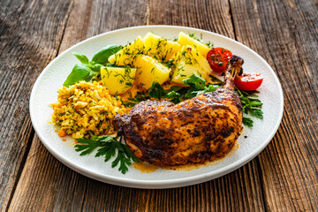 Oven roasted chicken leg with boiled potatoes and young cabbage salad on wooden table