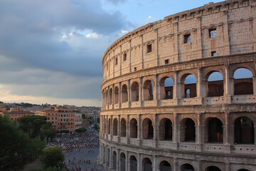 Fototapeta premium Colosseum in Rome stands majestically against epic sky, surrounded by ancient ruins and bustling crowds. historic architecture is beautifully illuminated by setting sun