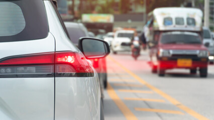 Rear side of white car with turn on brake light. Red light speed on tail light of car. Condition of busy cars on urban roads in Thailand.