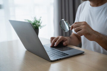 Close-Up of a Person Using a Laptop Computer with a Magnifying Glass in a Modern Workspace Setting with Natural Light and Indoor Plant