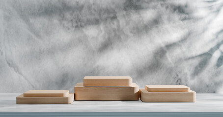 Minimalist scene with wooden podiums of different heights against textured gray background and soft leaf shadow, perfect for product display, branding, cosmetics, and elegant natural presentations. 3d