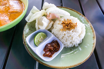 A delicious, complete meal of Minapadi chicken curry with rice, crackers, and chili sauce