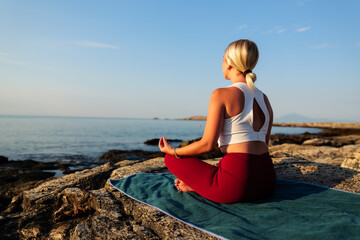 Young woman practicing yoga on a rocky coast at sunrise, finding inner peace and harmony with nature, enjoying a moment of mindfulness and meditation