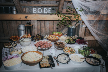 A rustic buffet table is filled with assorted traditional dishes, fresh salads, meats, and pastries, set in a cozy barn atmosphere.