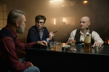 A group of men enjoying time playing cards in a dimly lit bar while sipping on drinks