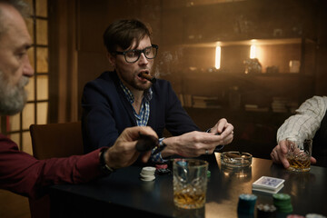 A group of men enjoying time playing cards in a dimly lit bar while sipping on drinks