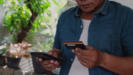 Asian man doing online shopping, typing credit card number on his mobile phone at home.
Cropped video shot of man making purchase and payment online via mobile phone. - Powered by Adobe
