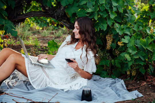 Woman with a glass of wine working on laptop in vineyard