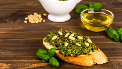 A toasted baguette topped with pesto and pine nuts, accompanied by olive oil and fresh basil, sits on a rustic wooden table.