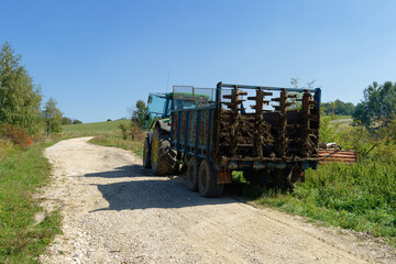 A tractor and trailer on a rural dirt road, transporting fertilizer under a clear blue sky.
