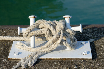 A weathered cleat secures a thick rope on a pier, ready for anchoring boats.