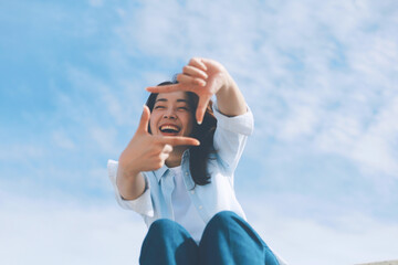 A cheerful woman wearing a casual shirt and jeans standing in front of the blue sky background with copy space.