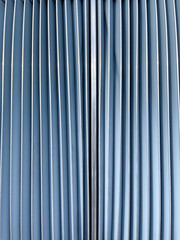 Obraz premium Close-up abstract view of blue metallic panels with vertical lines creating a symmetrical geometric pattern. Blue curved lines with metallic strip on a modern architectural background. 