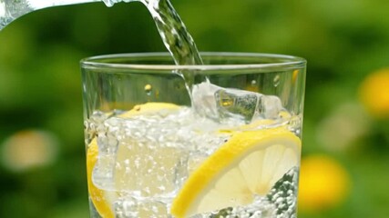 Water pours into a glass of water filled with lemon slices and ice - Powered by Adobe