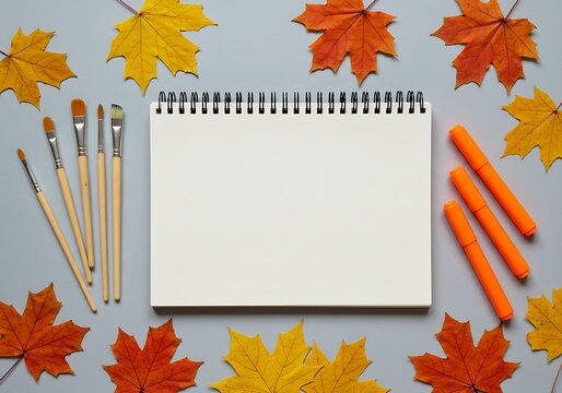 A seasonal theme for art and crafts, with a notebook, brushes, and fall leaves.