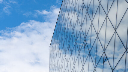 Fragment of a glass building with a reflecting blue sky with clouds. against its background. Modern offices in a skyscraper. High quality photo