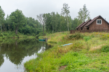 Obraz premium Summer village landscape. Houses on the green bank of the river and a fishing boat. High quality photo