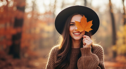 Woman in brown ribbed sweater and black hat holding orange maple leaf smiling in autumn setting. Cozy fall knitwear for comfort fashion brands, seasonal campaigns and warm autumn clothing collections