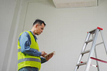 Construction worker checking plans with tablet while standing next to ladder in an empty room during renovation process for building improvement © pichet