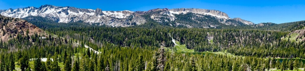 Wide panoramic vista in Mammoth, California, showing multiple ridgelines, extensive forest coverage, snow-capped summits, and classic Western American mountain range topography from elevated viewpoint