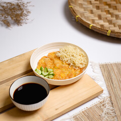 Serving of pempek telur goreng (fried fishcake omelet) with noodles and cucumber, accompanied by cuko vinegar sauce. Clean food styling for menu, recipe, and Asian cuisine content.