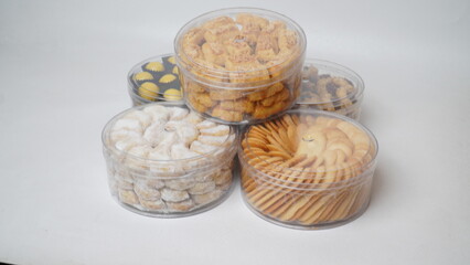Five transparent plastic jars filled with: Nastar, Kastengel, Lidah Kucing, Putri Salju, and Chocolate Thumbprint Cookies. Each jar is neatly arranged in a row and isolated on a clean white background
