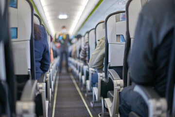 Passengers seated inside airplane cabin during flight journey with focus on aisle and seats.