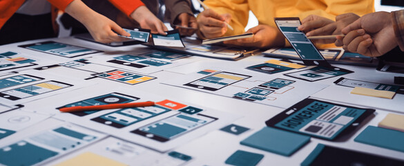 A diverse team engages in a dynamic design session, crafting wireframes and prototypes for mobile and web applications on a collaborative table filled with digital devices. SACTR