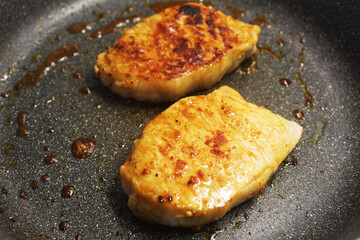 Two fried pieces of meat in a pan side view