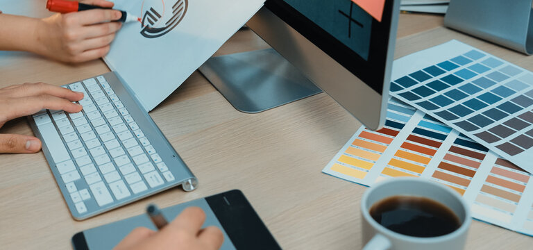 A dynamic office environment showcasing teamwork in action with hands busy on a keyboard, sketching on paper, and exploring color swatches for creative projects. SACTR