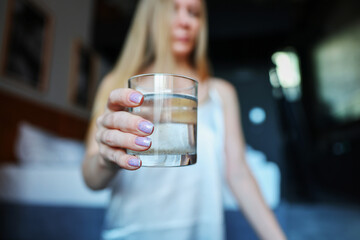 Woman holding a glass of fresh water with psyllium, focus on hand with pastel manicure.