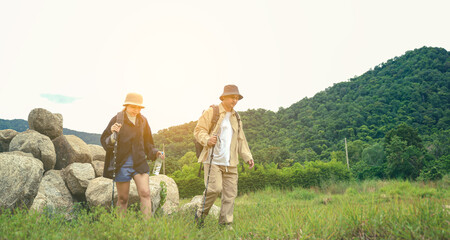 Active senior couple hiking on a trail through a lush green forest, enjoying outdoor nature, fitness, and adventure together.