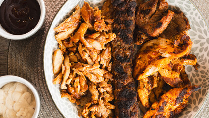 A beautifully arranged platter of grilled chicken shish, lamb shish, and doner kebab, served with vibrant sauces on the side. Elegant plating for food photography, menus, and promoting healthy, protei