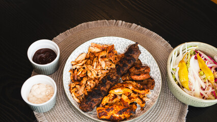 A beautifully arranged platter of grilled chicken shish, lamb shish, and doner kebab, served with vibrant sauces on the side. Elegant plating for food photography, menus, and promoting healthy, protei