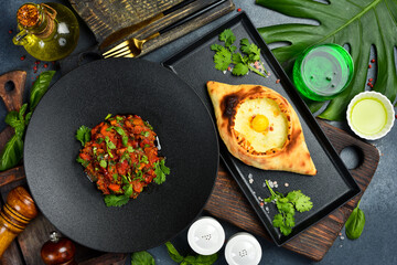 Georgian traditional food: khachapuri with cheese and egg and vegetable salad and a glass of tarragon drink. Top view.