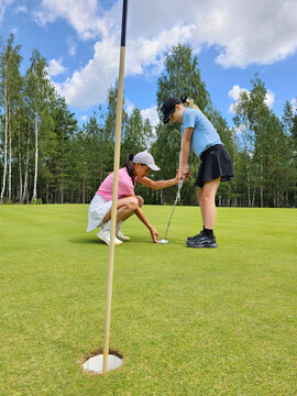 Golf instruction takes place on a sunny day ush green course with two players focused on putting technique