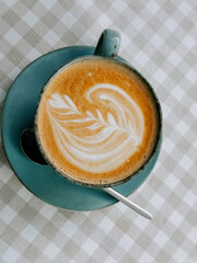 Delicious latte art served in a blue cup on a checkered tablecloth in a cozy cafe