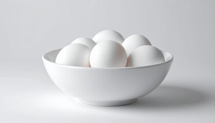 Minimalist composition featuring a white ceramic bowl filled with smooth white eggs, placed on a white surface with soft lighting and a monochromatic aesthetic.