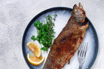 fried rainbow trout, with herbs and citrus fruits, on a plate, top view,