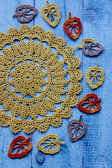Handmade crocheted autumn leaves arranged on vintage blue wooden surface. Ideal for creative design, fall decor, DIY inspiration, knitting tutorials, seasonal crafts, rustic background projects.
