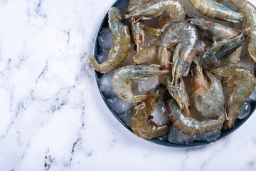 Fresh raw shrimp spread on ice with lemon and cilantro slices on a marble surface, ready to cook, no people