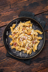 Italian Carbonara pasta topped with crispy bacon bits in a plate. Wooden background. Top view