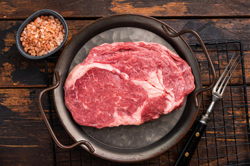 Prime Rib eye steak in a tray, raw dry aged beef meat on wooden background. top view