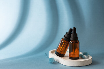 Two amber glass dropper bottles with cosmetic serum on blue background, rejuvenating cosmetic product, copy space