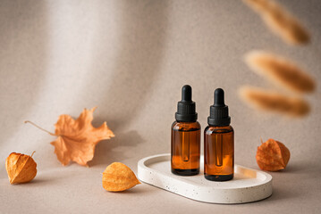 Amber glass dropper bottles with cosmetic serum or essential oil on beige background with autumn leaves, physalis, copy space, selective focus, skin care concept